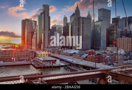 Skyline di New York dal ponte di Brooklyn al tramonto in inverno con nuvole nel cielo sullo sfondo Foto Stock