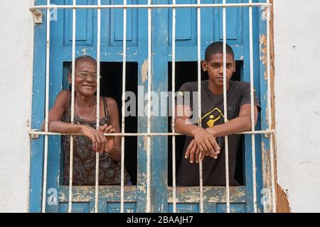 Nonna cubana e nipote che guardano attraverso le porte di legno blu intemperie e le finestre di ferro bar a Trinidad, Cuba Foto Stock
