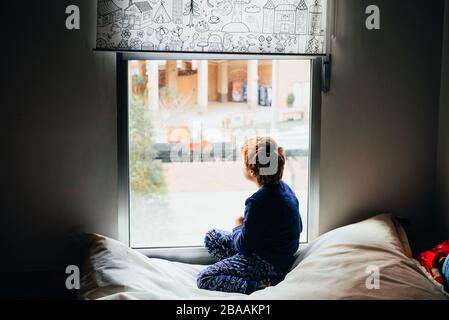 Triste e malinconico ragazzo guarda attraverso una finestra nel suo appartamento durante il suo confinamento Foto Stock