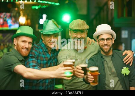 Ritratto di gruppo di amici che indossano cappelli e tostano con birra mentre sorridono a macchina fotografica e celebrano la vacanza Foto Stock