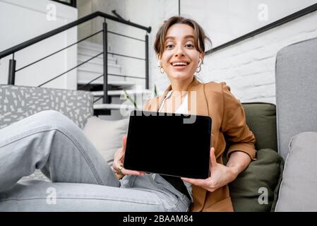 Donna giovane e allegra con un tablet digitale a casa. Tablet con schermo nero per copiare spazio Foto Stock