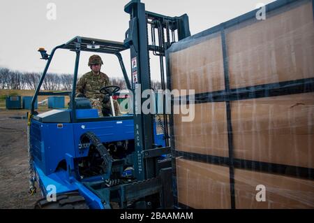 Un soldato della Guardia Nazionale del Connecticut utilizza un carrello elevatore a forche per trasportare un pallet di letti portatili e biancheria a un camion rimorchio trattore da distribuire agli ospedali del campo mobile a supporto del COVID-19, risposta coronavirus 25 marzo 2020 a New Haven, Connecticut. Foto Stock