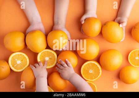 Tangerini nelle mani dei bambini si avvicinano sopra lo sfondo delle arance Foto Stock