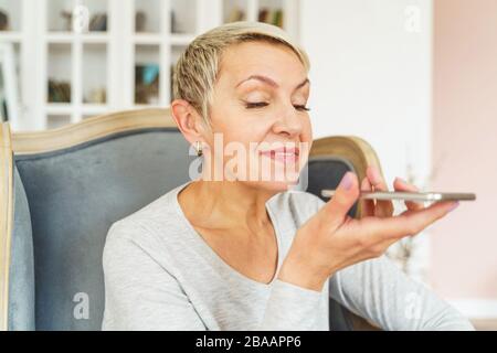 Signora gioiosa che usa il suo smartphone a casa Foto Stock