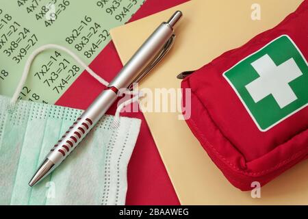 Penna, maschera medica e kit di pronto soccorso su un notebook della scuola. Concetto di prevenzione delle malattie. Concetto di rischio di infezione e diffusione del virus. Foto Stock