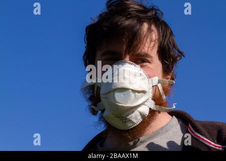 Giovane uomo caucasico che indossa una maschera facciale davanti a un cielo blu Foto Stock