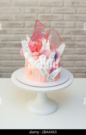 Moderna ed elegante torta rosa con caramello, cioccolato bianco, carta da waffle, meringhe e macaroon francesi decorati su cakestand bianco. Foto Stock