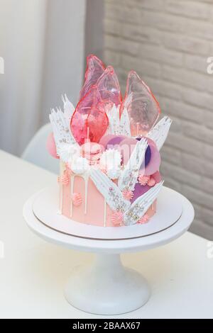 Moderna ed elegante torta rosa con caramello, cioccolato bianco, carta da waffle, meringhe e macaroon francesi decorati su cakestand bianco. Foto Stock