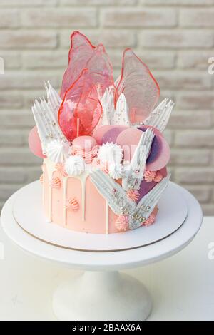 Moderna ed elegante torta rosa con caramello, cioccolato bianco, carta da waffle, meringhe e macaroon francesi decorati su cakestand bianco. Foto Stock