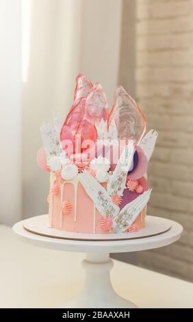 Moderna ed elegante torta rosa con caramello, cioccolato bianco, carta da waffle, meringhe e macaroon francesi decorati su cakestand bianco. Foto Stock