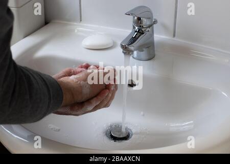 Dettaglio di un giovane maschio che lava le mani con sapone sotto acqua corrente per ridurre il rischio di infezione durante la pandemia di virus corona Foto Stock