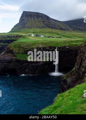 Isole Faroe, famosa cascata di Mulafossur, la sua acqua che cade nell'oceano. Sopra c'è un villaggio Gasadalur. Foto Stock