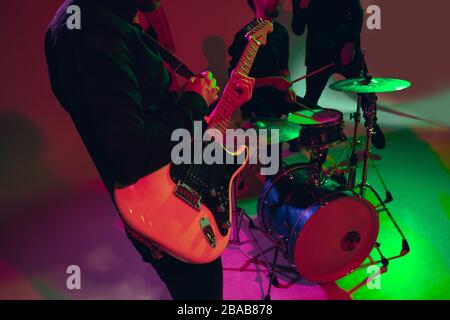 Giovane e gioioso musicista caucasico che si esibisce su sfondo rosso alla luce del neon. Concetto di musica, hobby, festival. Ritratto colorato di artista moderno. Attenuto, ispirato. Art, fascia di copertura. Primo piano. Foto Stock