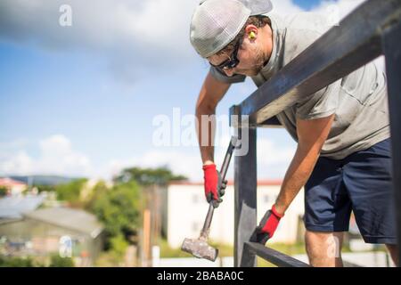 Lavoratore di costruzione che usa il martello per costruire la ringhiera di acciaio sul tetto. Foto Stock