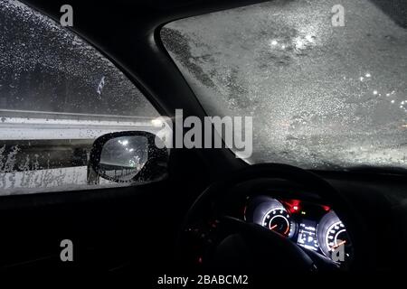 Ghiaccio e neve sul parabrezza ghiacciato dell'automobile sulla strada notturna Foto Stock