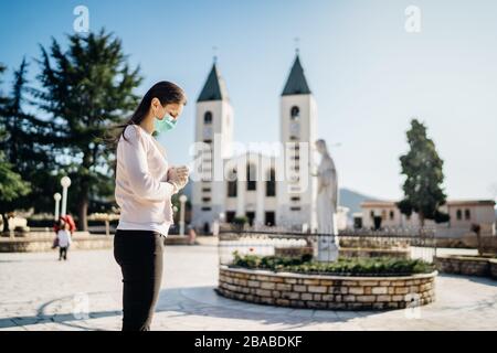 Donna che indossa maschera e guanti in preghiera a Dio a causa del romanzo coronavirus covid-19 focolaio in Medjugorje.Woman in stress emotivo e pain.Christianity. Foto Stock