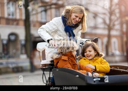 Madre che controlla i suoi bambini che sta guidando nella sezione anteriore di una bici di carico Foto Stock