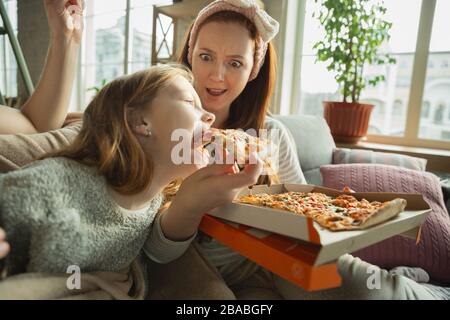 La famiglia che trascorre un bel tempo insieme a casa, sembra felice e allegra. Mamma, papà e figlia che si divertono, mangiano la pizza, guardando la partita sportiva o la TV. Insieme, conforto domestico, amore, concetto di relazioni. Foto Stock