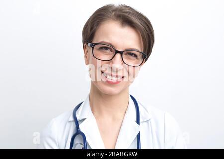 Ritratto di una donna sorridente in camice da laboratorio con stetoscopio su sfondo bianco. Foto Stock
