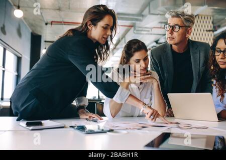 Designer che dà alcune nuove idee sul progetto al suo team in riunione. Persone aziendali che parlano di un nuovo progetto aziendale in ufficio. Foto Stock