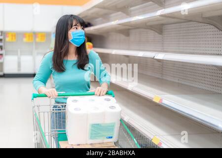Donna asiatica che guarda Supermarket vuoto carta igienica scaffali in mezzo COVID-19 Coronavirus paure, acquirenti panico acquisto e stoccaggio carta igienica preparazione Foto Stock
