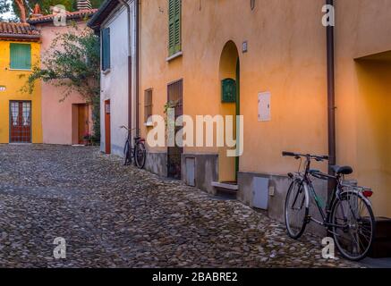 Vista su una tranquilla strada medievale del centro con case colorate dietro le mura medievali della città di Cesena con ciottoli e una vecchia bicicletta in Italia Foto Stock