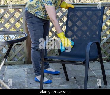 Una donna pulisce una sedia da giardino in rete con un panno in microfibra. Indossa guanti di gomma gialli. Foto Stock