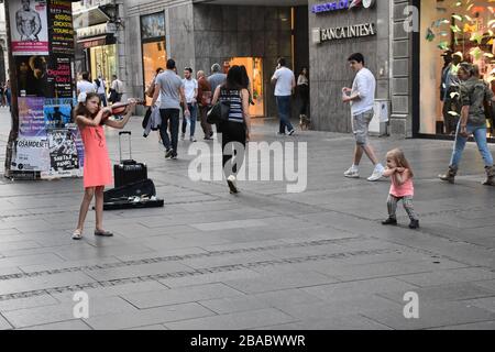 Sul lungomare principale di Belgrado, una ragazza in abito arancione suona un violino. Gli escursionisti passano accanto a lei Foto Stock