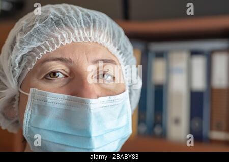 Medico stanco in maschera protettiva e cappuccio contro il coronavirus tipo Covid 19. Primo piano. Foto Stock