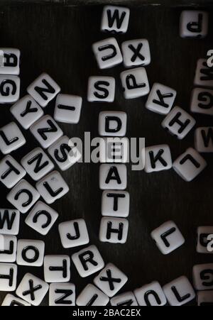 Ancora la vita che mostra blocchi di lettera in bianco e nero che ortografano la morte di parola fra altri blocchi di lettera contro uno sfondo nero Foto Stock