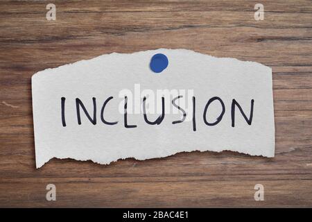 Parola di inclusione scritta su carta strappata. Testo su tavola di legno. Foto Stock