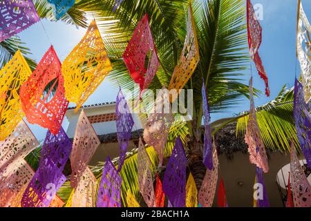 Arte popolare messicana, papel picado, appeso su una strada fiancheggiata da palme a metà giornata sole, Sayulita, Riviera Nayarit, Nayarit, Messico. Foto Stock