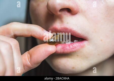 Colpo di primo piano di una pillola tra i denti di una donna Foto Stock