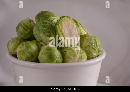 Piccola ciotola bianca piena di germogli di bruxelles lavati. Foto Stock