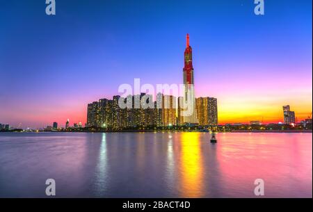 Il colorato paesaggio del tramonto in un'area urbana lungo il fiume con grattacieli che mostrano lo sviluppo più economico nella città di ho Chi Minh, in Vietnam Foto Stock