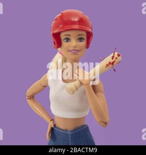 Bambola che tiene una mazza da baseball con unghie sotto le luci su sfondo viola Foto Stock