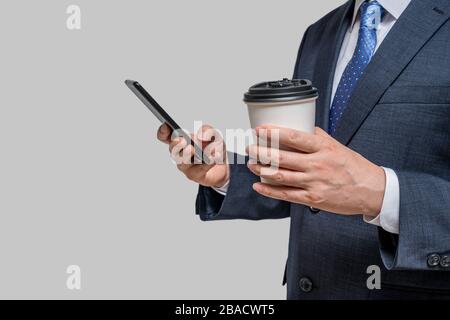 Un uomo d'affari che ha in mano una tazza di carta bianca e uno smartphone. Con spazio di copia. Foto Stock