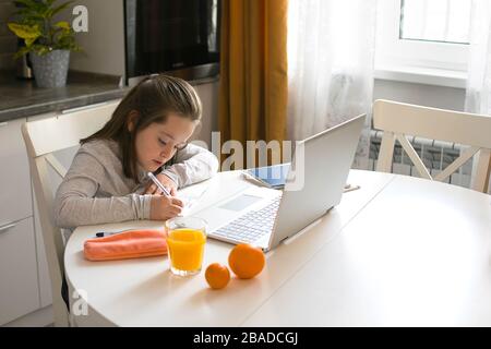 Bella schoolgirl carino studiare a casa utilizzando il computer portatile. Coronavirus scuola domestica, istruzione online, istruzione domestica, concetto di quarantena. Ti sentirai come a casa Foto Stock