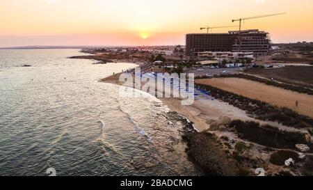 Vista aerea del tramonto sulla costa e della spiaggia simbolo di Agia Thekla, Ayia Napa, Famagosta, Cipro dall'alto. Vista dello skyline dall'alto dell'attrazione turistica Foto Stock