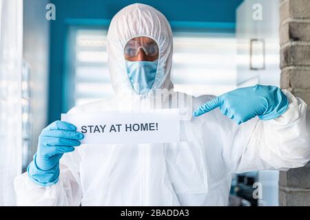 Uomo in tuta anti virus protettiva e maschera di tenuta con messaggio rimanere a casa Foto Stock