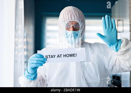 Uomo in tuta anti virus protettiva e maschera di tenuta con messaggio rimanere a casa Foto Stock