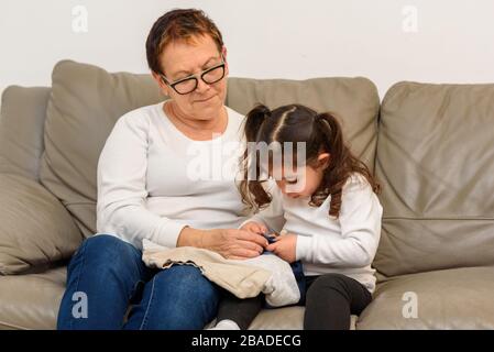 La nonna insegna a sua nipote di mettere i vestiti. La ragazza del toddler sullo studio domestico a causa di focolaio di Covid 19. Foto Stock