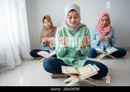 Tre donne asiatiche si siedono e pregano per rendere grazie a Dio mentre imparano a recitare il Santo Corano insieme nella casa Foto Stock