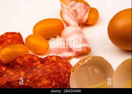 Uova di pollo spezzate, fette di pancetta e salsiccia e pomodori su sfondo bianco. Primo piano Foto Stock