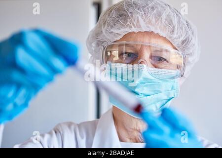 Virologo con indumenti protettivi e campione di sangue per il test Covid-19 in laboratorio Foto Stock