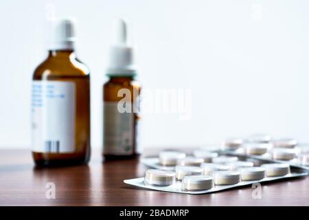 Fotografia di closeup della confezione blister con compresse, flaconcini o gocce sul piano del tavolo in legno marrone. Sfondo bianco sfocato e spazio per il testo. Foto Stock