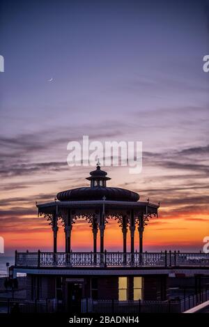 Brighton, Regno Unito, 26 Mar 2020, il sole tramonta dietro la bandstand sul lungomare di Hove questa sera, mentre il paese si isola contro il coronavirus. Foto Stock