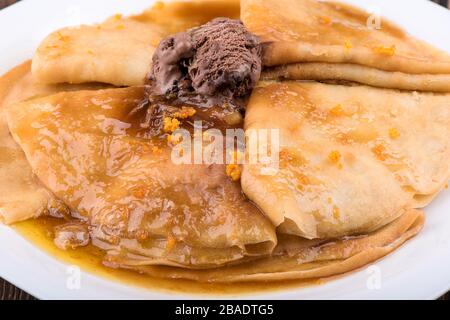 Istantanea macro. Pancake con salsa dolce e gelato al cioccolato su un piatto bianco. Piatto con frittelle su un tavolo di legno. Foto Stock