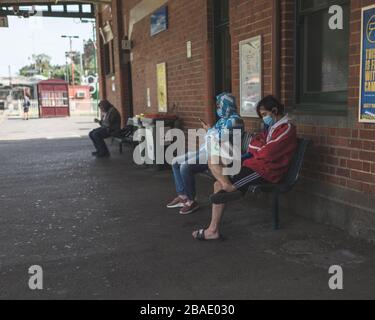 MELBOURNE - MAR. 21, 2020: I pendolari che indossano maschere protettive attendono in una stazione ferroviaria quasi vuota della città durante il nuovo focolaio di coronavirus. Foto Stock