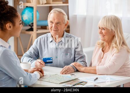 Agente di viaggio in ufficio seduto con i clienti senior uomo dando carta di credito fiducioso Foto Stock
